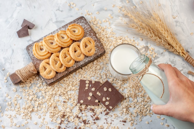 도마에 있는 다양한 비스킷 초콜릿 밀 스파이크 손으로 회색 배경에 흩어져 있는 귀리에 우유를 붓는