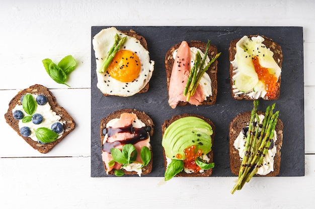 Top view of various bruschettas,sandwiches with different healthy fillihgs served on dark plate