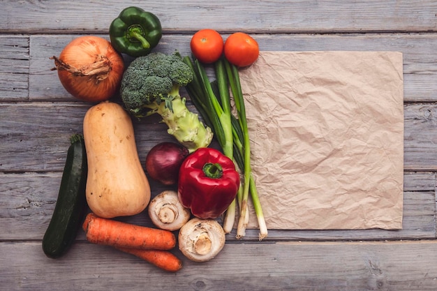 Top view of various fresh organic vegetables with a blank brown paper bag