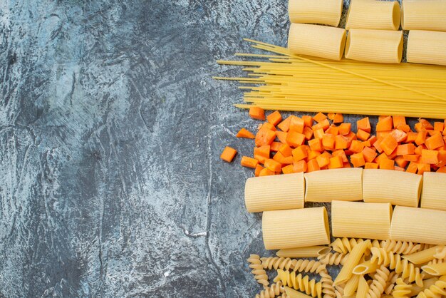 top view various pastas rigatoni spaghetti penne spirals chopped carrot on grey background with free space