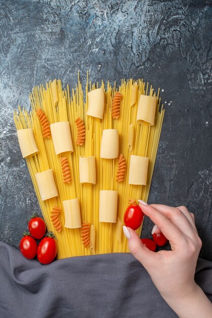 Top view various pastas rigatoni spaghetti spirals cherry\
tomato in female hand purple shawl on grey background