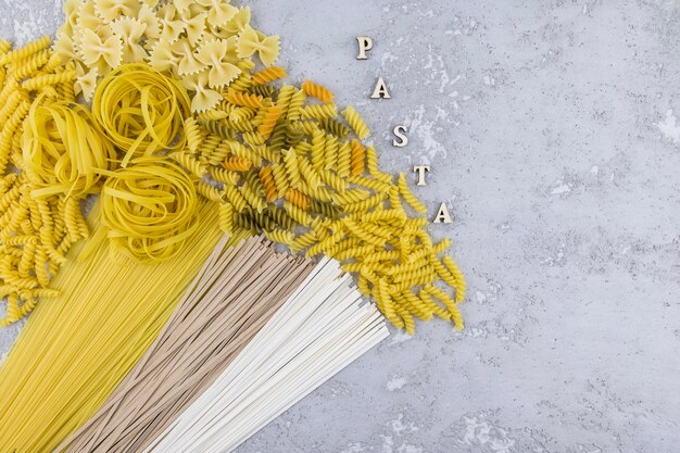 Photo top view of various types of dry pasta and noodles on a grey background. letters - paste.