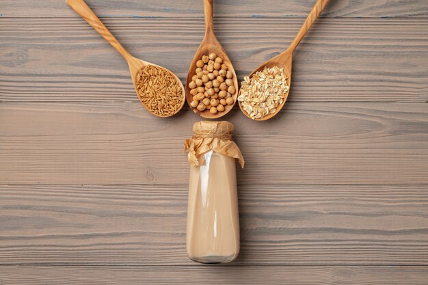 Top view of vegan milk and grains in wooden spoons on wooden surface copy space