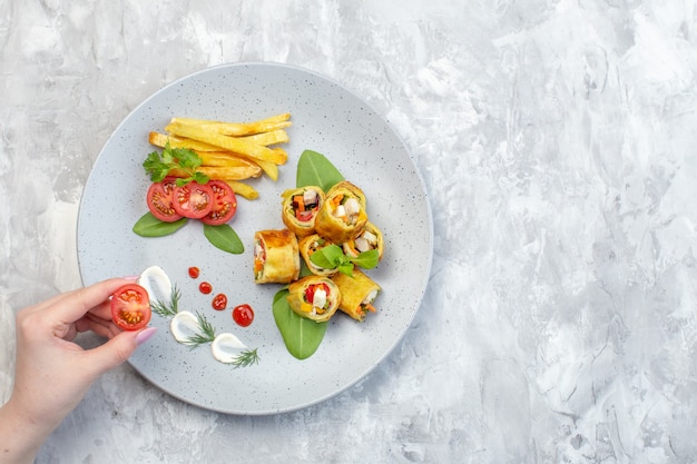 Vista dall'alto patè di verdure rotoli con pomodori e patatine fritte all'interno della piastra sulla superficie bianca