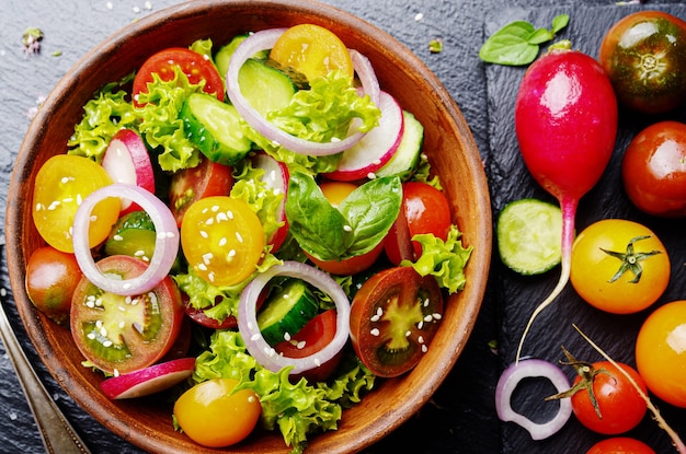 Top view at vegetable salad of lettuce cherry tomatoes radish cucumber onion and basil on slate stone tray