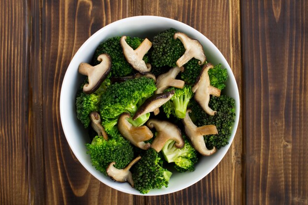 Top view of vegetarian salad with mushrooms shiitake and broccoli in the white bowl on the wooden