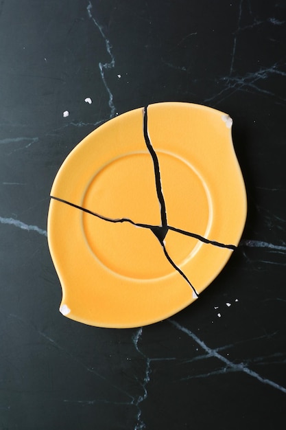 Top View of Vibrant Yellow Broken Ceramic Coaster on Black Marble Countertop