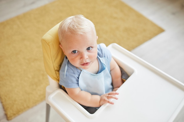 top view of view shot of little toddler wearing bib sitting on high chair waiting for meal