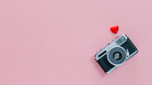 Top view of vintage old camera and little red heart on pink pastel background.