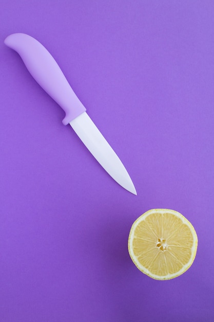 Top view of violet knife and half lemon on the violet surface