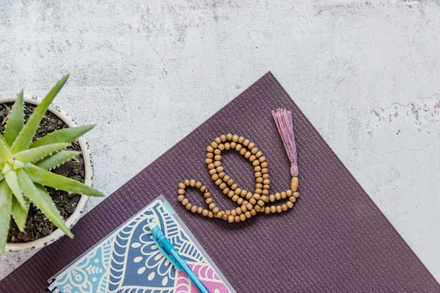 Photo top view of a violet yoga mat, bad wooden beads on white background. essential accessories for practice yoga and meditation. copy space