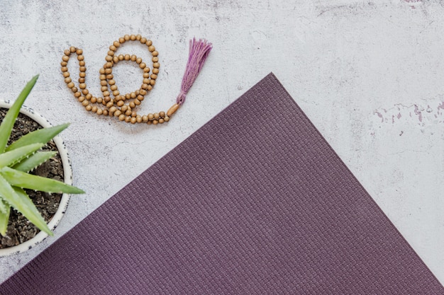 Top view of a violet yoga mat, bad wooden beads on white background. Essential accessories for practice yoga and meditation. Copy space