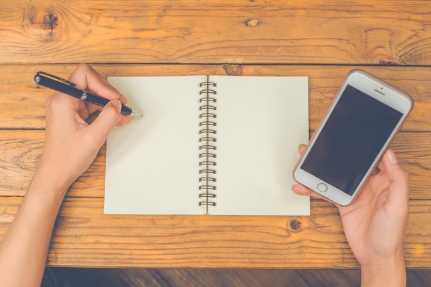 Foto top view vrouw hand schrijft op een leeg notitieboekje met een pen op een houten achtergrond