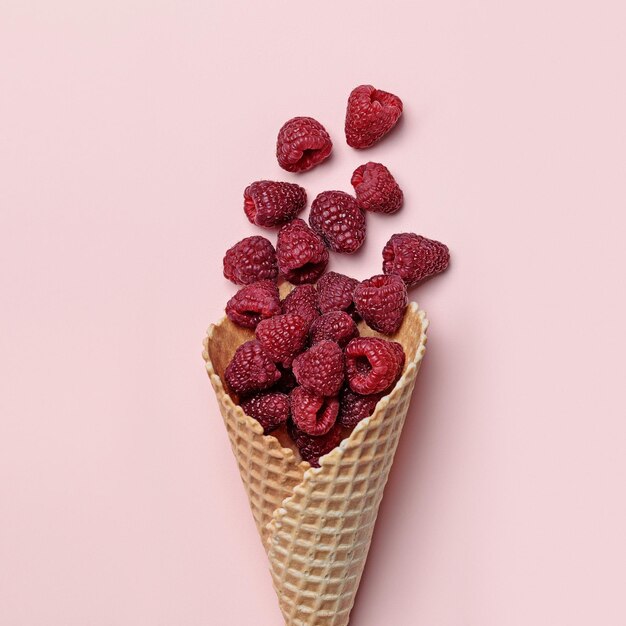 Top view of waffle cone with ripe raspberries on pastel coral background, flat lay