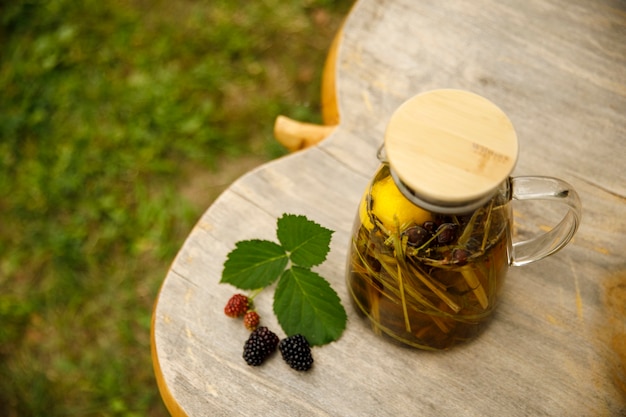 Top view of a warm glass teapot, green tea leaves and lemongrass on the wooden desk at autumn day.