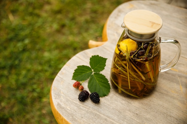 Top view of a warm glass teapot, green tea leaves and lemongrass on the wooden desk at fall day. Closeup image.