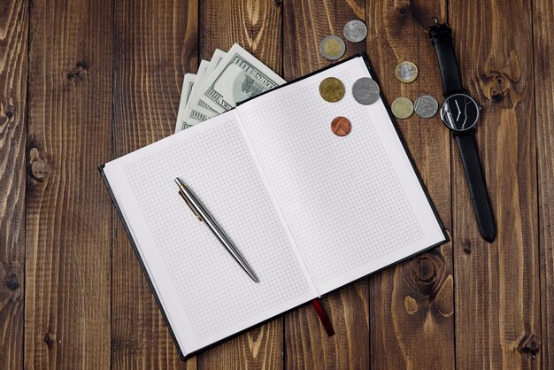 Top view of watch, pen, open notebook, banknotes and coins