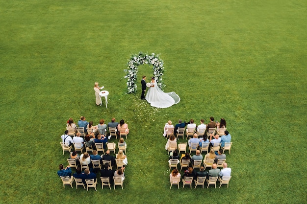 Top view of the Wedding ceremony in a green field with guests sitting on chairs. Wedding venue on the green lawn.