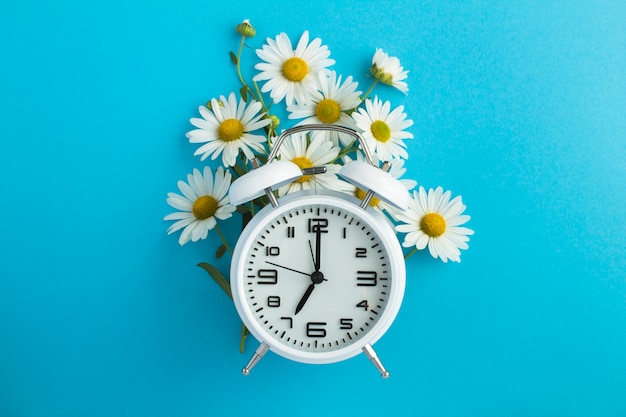 Top view of white alarm clock and bouquet of chamomiles