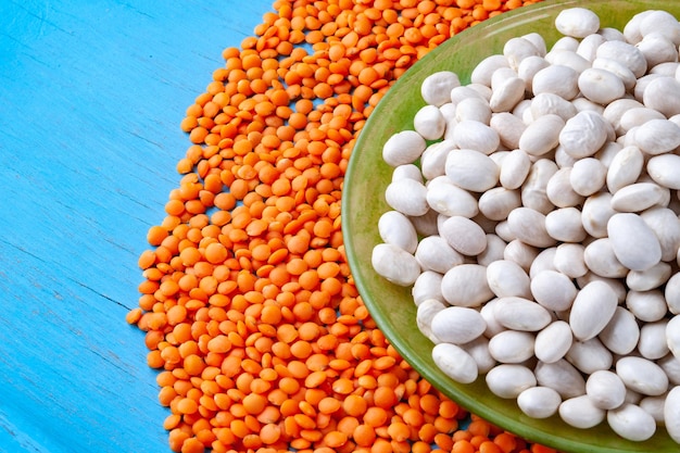 Top view white beans in a green plate and red lentils on a blue wooden background