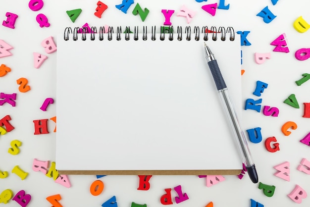 Top view of a white blank notepad with a pen and colored english letters The concept of study lessons back to school