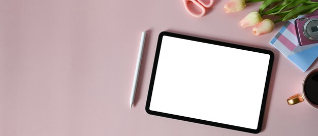 Photo the top view of a white blank screen computer tablet is putting on a table surrounded by various feminine equipment.
