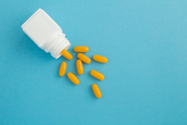 Top view of white bottle with the yellow pills on blue