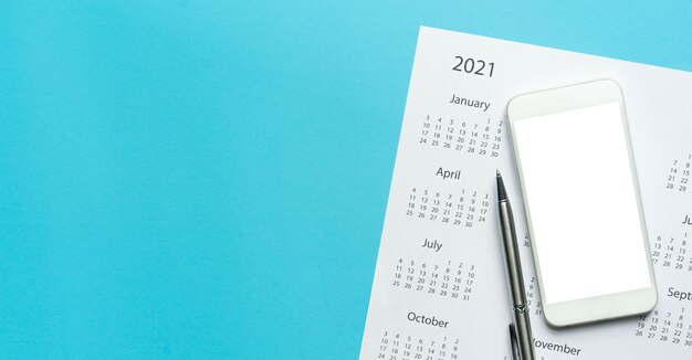 Вид сверху на белый календарь 2021 года с пустым экраном смартфона на синем фоне