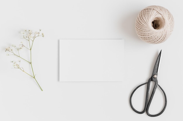 Top view of a white card mockup with a gypsophila and workspace accessories on a white table