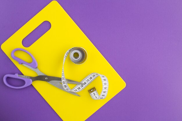 Top view of white centimeter and scissors on the yellow cutting board