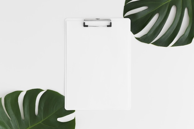 Top view of a white clipboard mockup with monstera leaf decoration on a white table