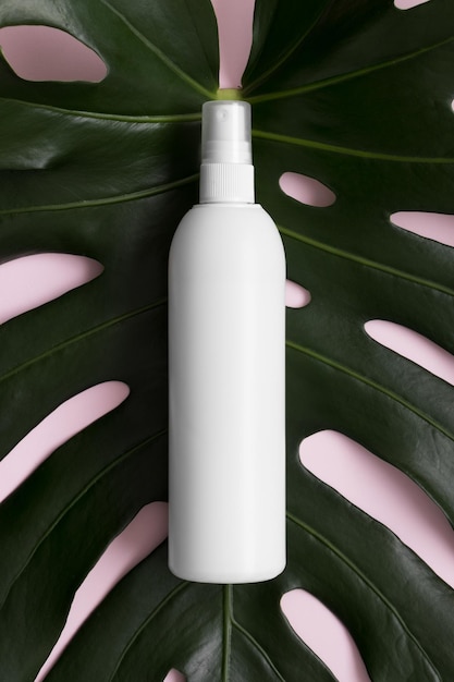Top view of a white cosmetic spray bottle mockup with a monstera leaf on a pink background