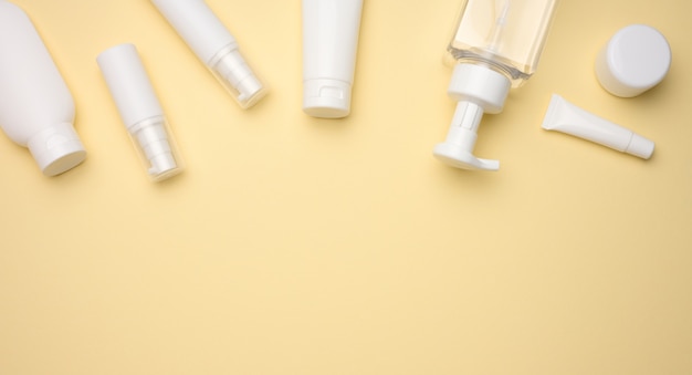 白いクリーム色のチューブ、化粧品ディスペンサー、空の瓶とハンドクリーム、明るい黄色の背景に透明なディスペンサーの上面図。化粧品のブランディング、モックアップ