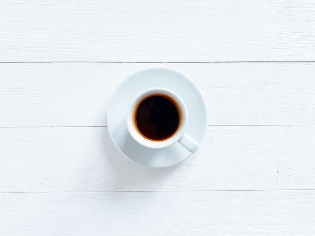 Vista superiore della tazza bianca di caffè nero o cioccolata calda sulla tavola di legno squallida del bordo bianco.