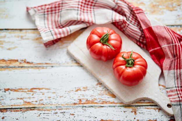 Top view of a white cutting board with a fresh juicy tomatoes on a wooden rustical table