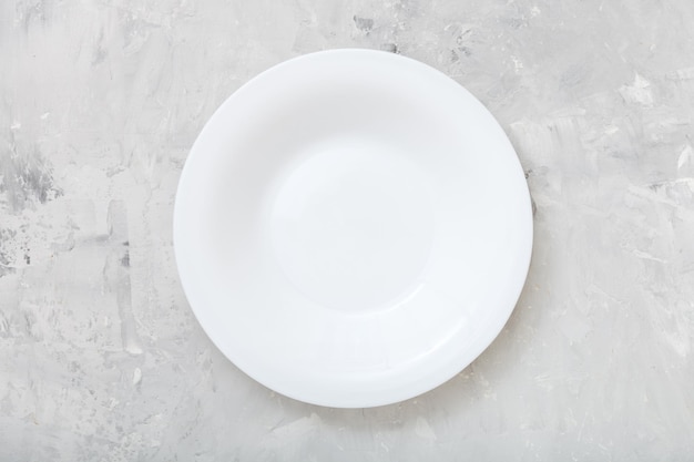 Вид сверху на белую глубокую тарелку на бетонной доске