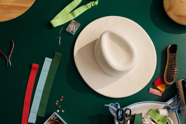 Top view of white felt hat among variety of textile samples and other supplies