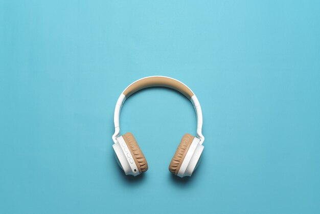 Top view of white headphones on blue background with copy space. Flat lay.