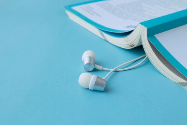 Vista dall'alto di cuffie e notebook bianchi su sfondo blu con spazio per la copia audiolibro piatto