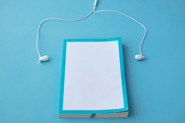 Top view of white headphones and notebooks on blue background with copy space Flat lay Audio book