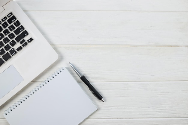 Top view of white laptop with blank white notepad and pen copy space