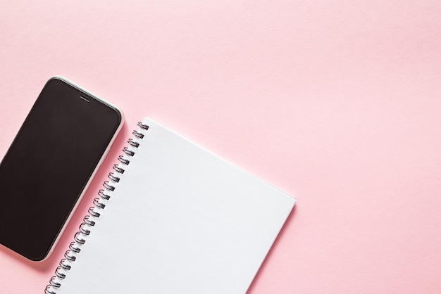 Top view white notepad and smartphone on pink background with copy space