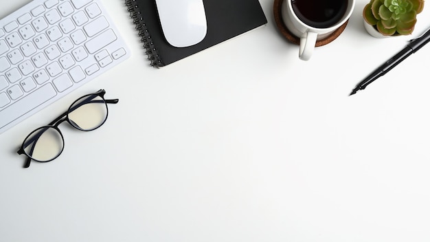 커피 컵, 안경, 키보드, 노트북 및 복사 공간이 있는 흰색 사무실 책상의 상단 전망.
