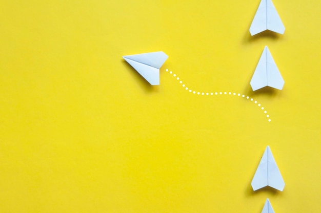 Foto vista dall'alto degli origami dell'aeroplano di carta bianca che lasciano un altro aeroplano bianco su sfondo giallo con spazio personalizzabile per testo o idee copia spazio