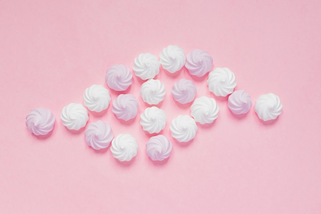 Top view of white and pink twisted meringues  on pink background