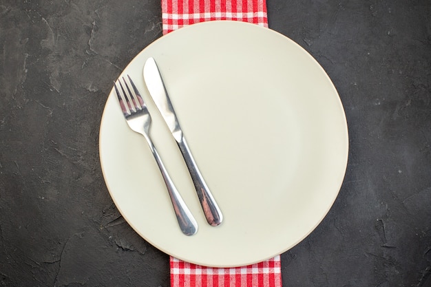 Top view white plate with fork and knife on dark surface