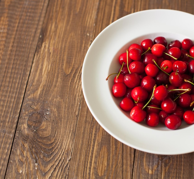 Top view of white plate with fresh red cherries on the brown wooden table