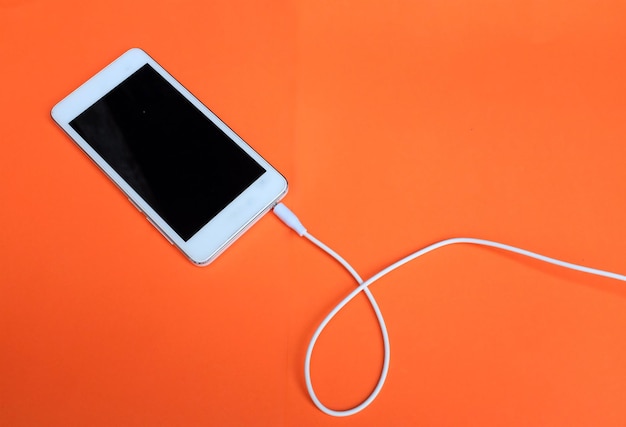 オレンジ色の背景に白いスマートフォンとイヤホンをトップビュー