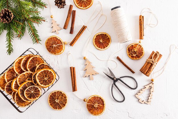 Photo top view of white textured background with homemade garland of dried oranges spruce branches orange slices and craft scissors flat lay decoration