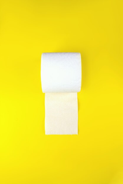 Top view of white toilet paper rolls on yellow background with copy space.